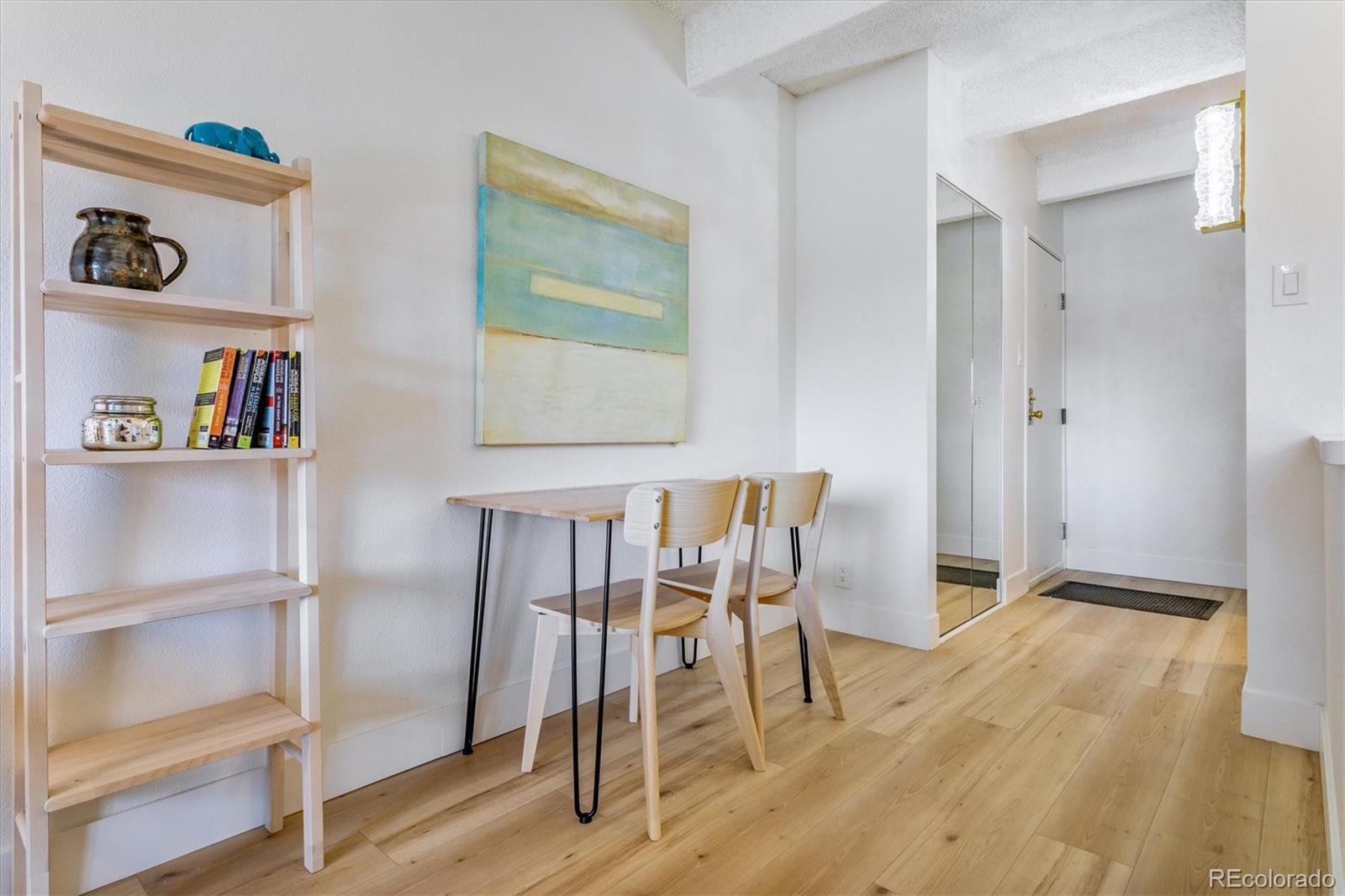 Dining nook with a light wood table, open shelving, and a mirrored entry closet.