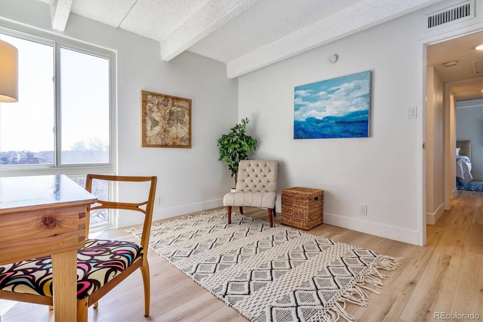 Furnished dining and sitting area with a large window, patterned rug, and pale wood floors.