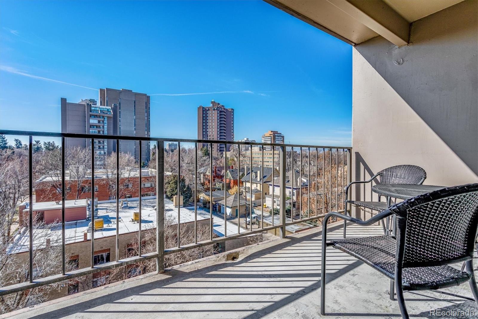Apartment balcony with woven chairs overlooking Denver high-rises and snow-dusted rooftops.