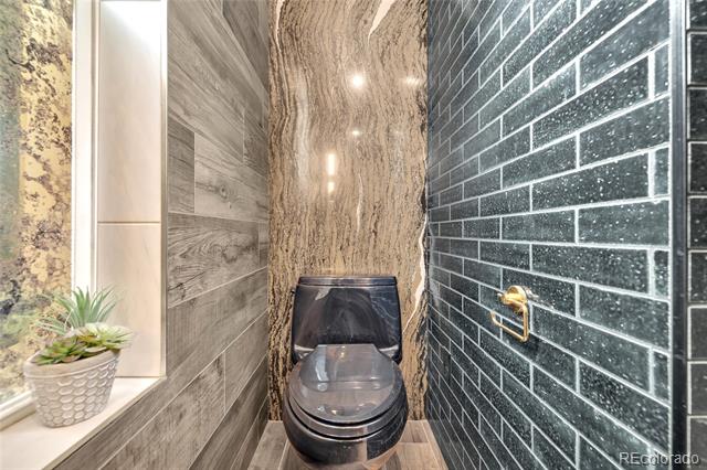 Modern bathroom with a dark toilet, glossy charcoal tile, and warm wood-look walls.
