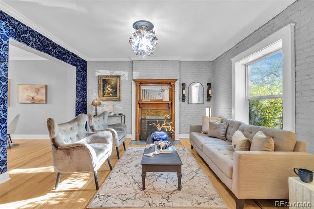 Living room with a brick fireplace, blue patterned accent wall, tufted armchair, and sunlit window.