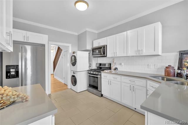 Kitchen with white cabinetry, gray countertops, stainless steel appliances, and a washer and dryer beside the refrigerator.