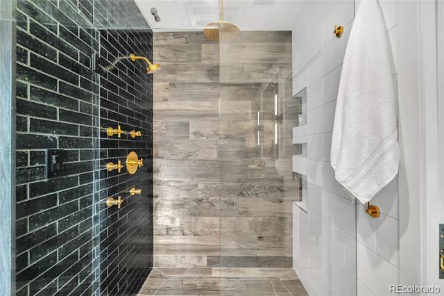 Walk-in shower with black tile, gold fixtures, and gray stone walls.