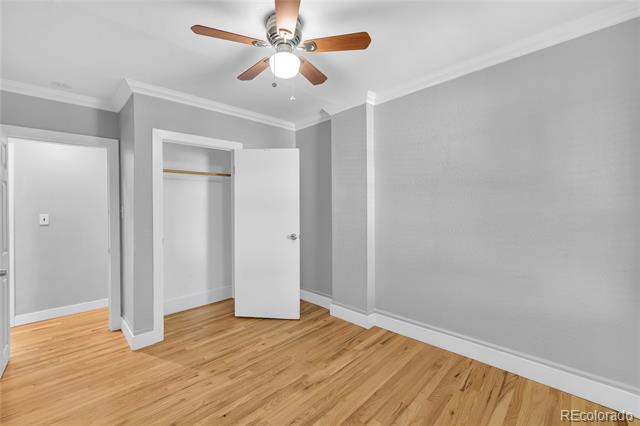 Empty bedroom with gray walls, light wood floors, an open closet, and a wooden-blade ceiling fan.