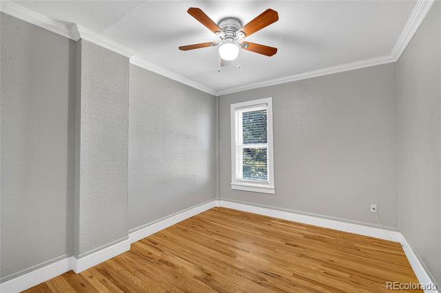 Empty room with hardwood floors, gray walls, a window, and a wood-blade ceiling fan.