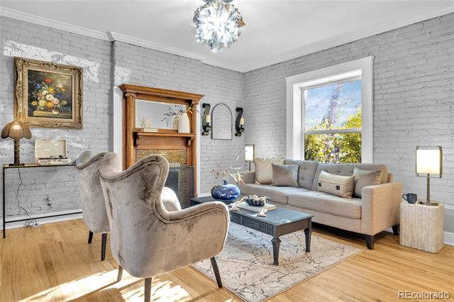 Living room with a beige sofa, painted brick walls, a wood-mantel fireplace, and sunlit hardwood floors.