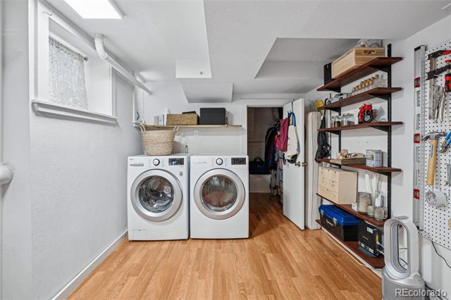 Laundry room with front-loading washer and dryer, wood flooring, and open storage shelves.