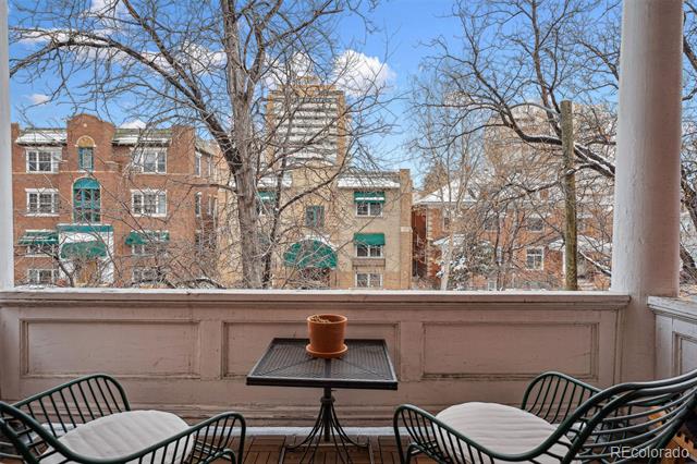 Covered porch with metal chairs and a table overlooking brick buildings and leafless trees.