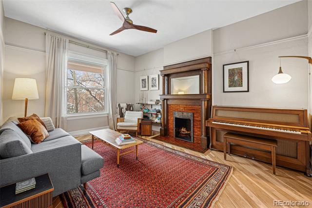 Living room with a wood-burning fireplace, upright piano, and red patterned rug.