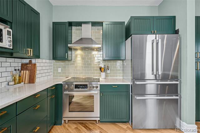 Kitchen with dark green cabinets, subway tile backsplash, and stainless steel appliances.