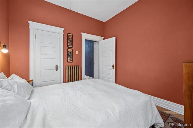Bedroom with terracotta walls, a white bed, paneled doors, and a vintage radiator.