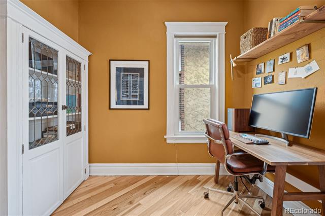Home office with ochre walls, a wood desk and shelves, and white glass-front cabinets.