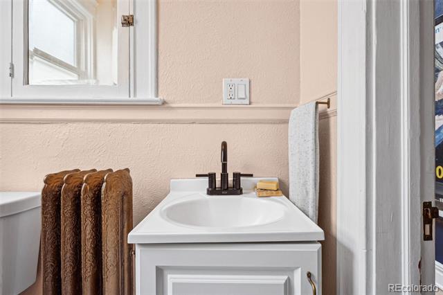Bathroom vanity with a white sink, dark faucet, and cast-iron radiator beside a window.