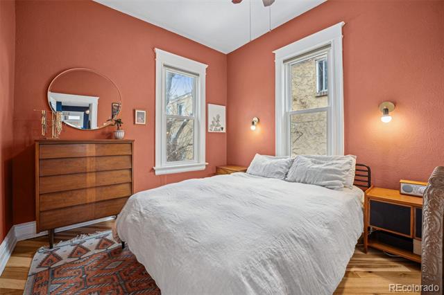 Bedroom with coral walls, a white bed, two tall windows, and a wooden dresser.