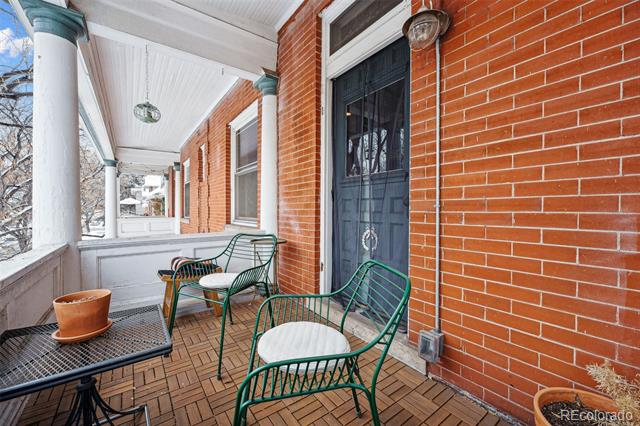 Covered brick front porch with green metal chairs, a dark entry door, and snow visible outside.