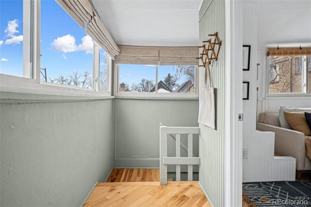 Enclosed sunroom with large windows, pale green walls, and warm wood floors.