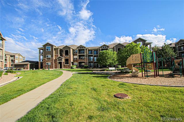 Apartment building exterior with landscaped lawn, curved walkway, and playground.
