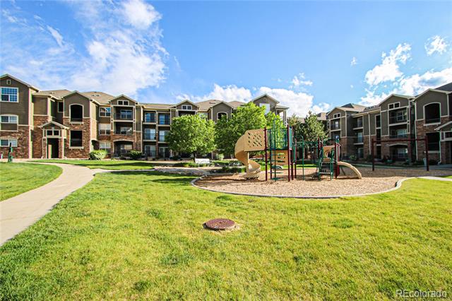 Apartment complex courtyard with a playground, green lawn, and curving walkway.