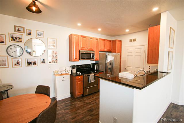 Condo kitchen with reddish wood cabinets, stainless steel appliances, and a peninsula beside a round dining table.