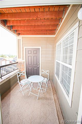 Covered balcony with exposed reddish beams, a dark entry door, and a small white table and chairs.
