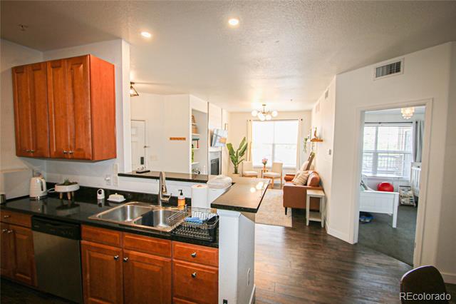 Condo kitchen with reddish wood cabinets and black countertops opening to a furnished living area.