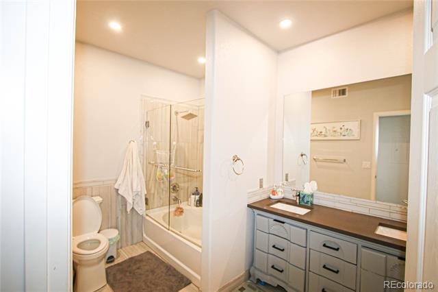 Bathroom with a gray double vanity, dark countertop, and glass-enclosed tub and shower.