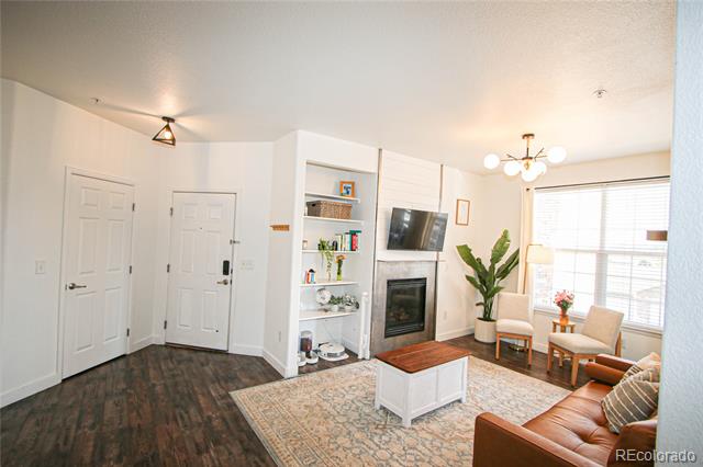 Living room with a fireplace, built-in shelves, dark wood floors, and a large window with blinds.