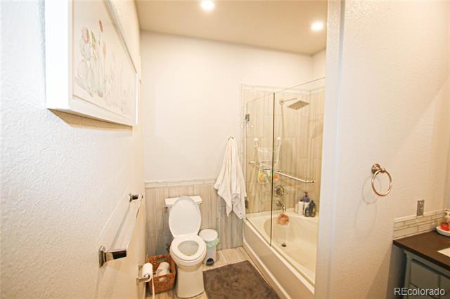 Bathroom with a glass-enclosed tub and shower, toilet, and tiled wainscoting.