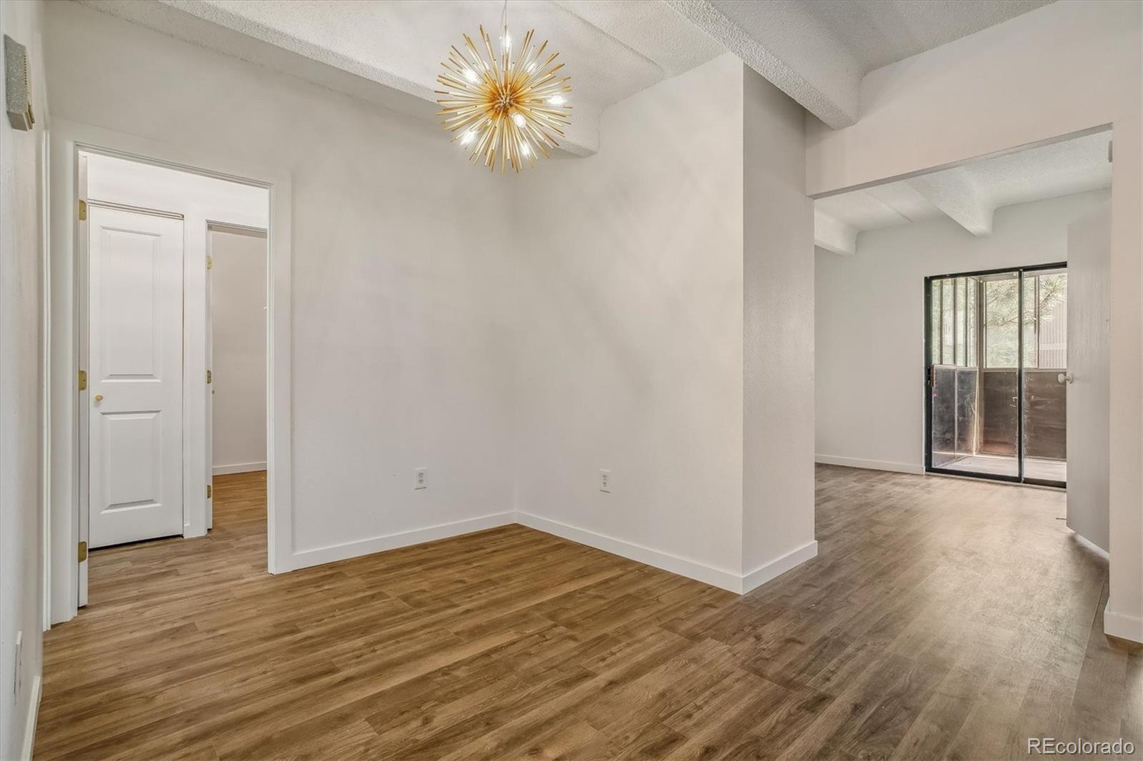 Open living and dining area with wood-look floors, a starburst chandelier, and sliding glass doors to a patio.