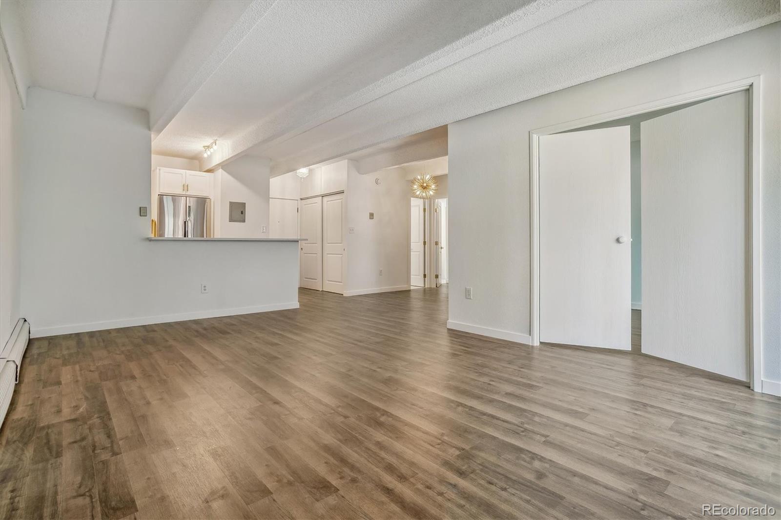 Unfurnished condo living area with wood-look floors, white kitchen cabinets, and sliding closet doors.