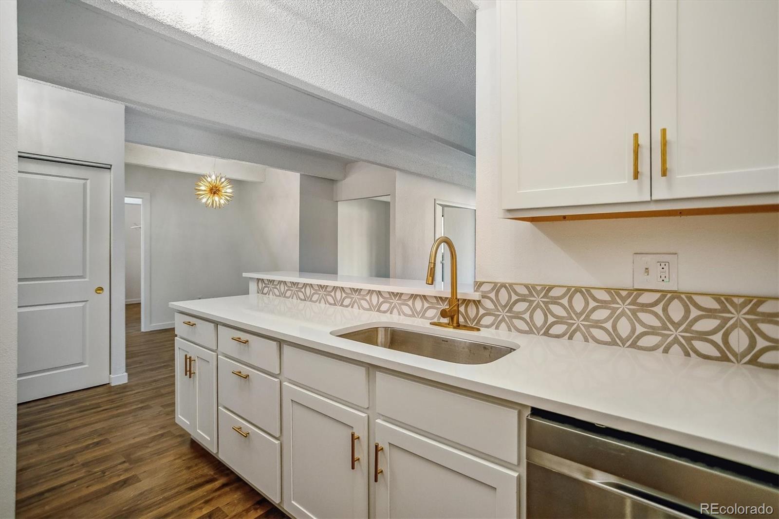 Kitchen with white cabinets, gold fixtures, patterned backsplash, and dark wood-look flooring.