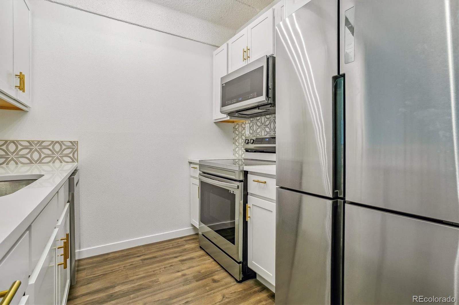 Kitchen with white cabinets, geometric tile backsplash, gold hardware, and stainless-steel appliances.