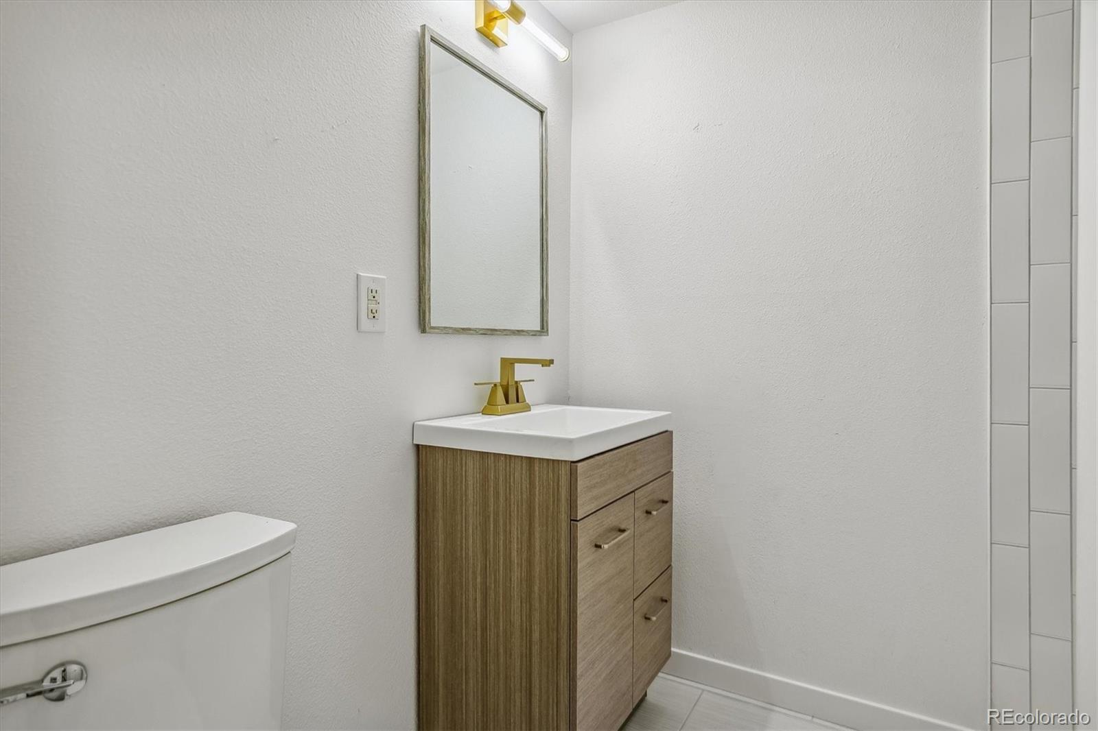 Bathroom vanity with a gold faucet and framed mirror, beside a partially visible toilet and tiled shower.