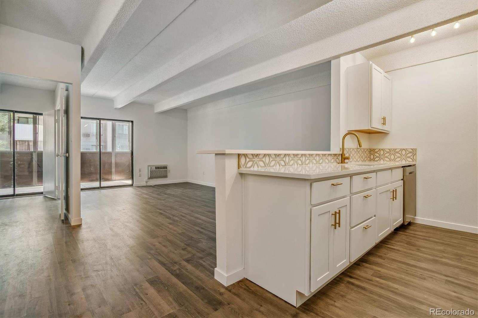 Open kitchen with white cabinets and gold hardware overlooking a living area with sliding glass doors.