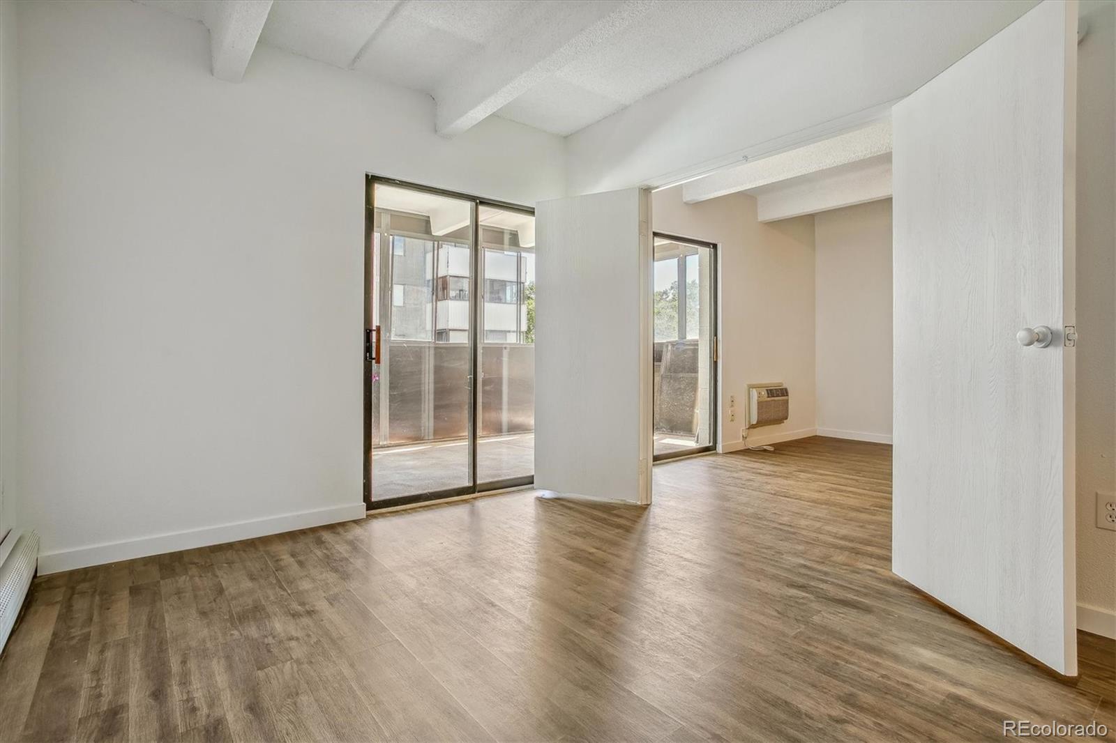Empty condo living area with wood-look floors and sliding glass doors to a balcony.