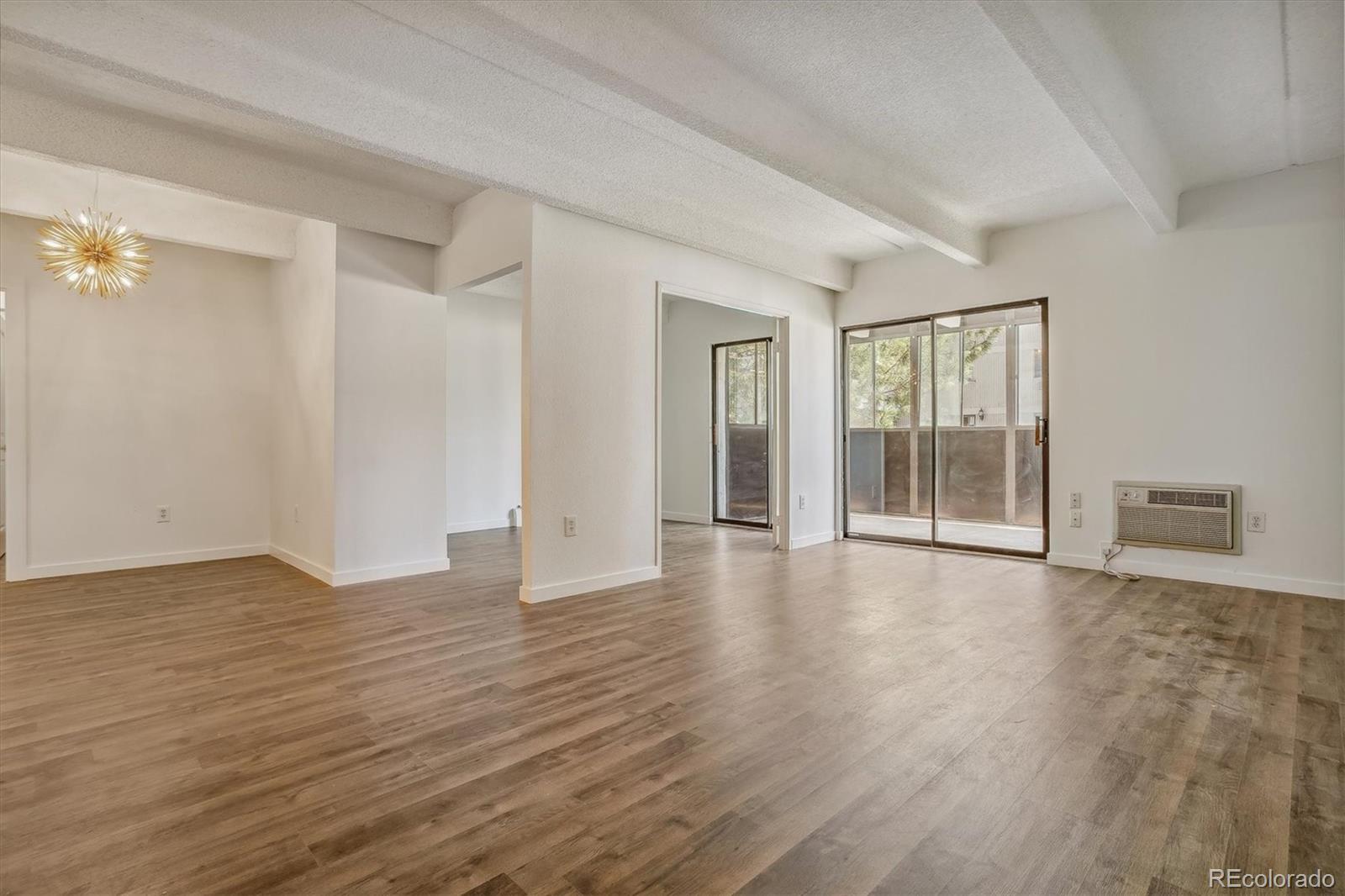 Empty living and dining area with wood-look flooring and sliding glass doors to a balcony.