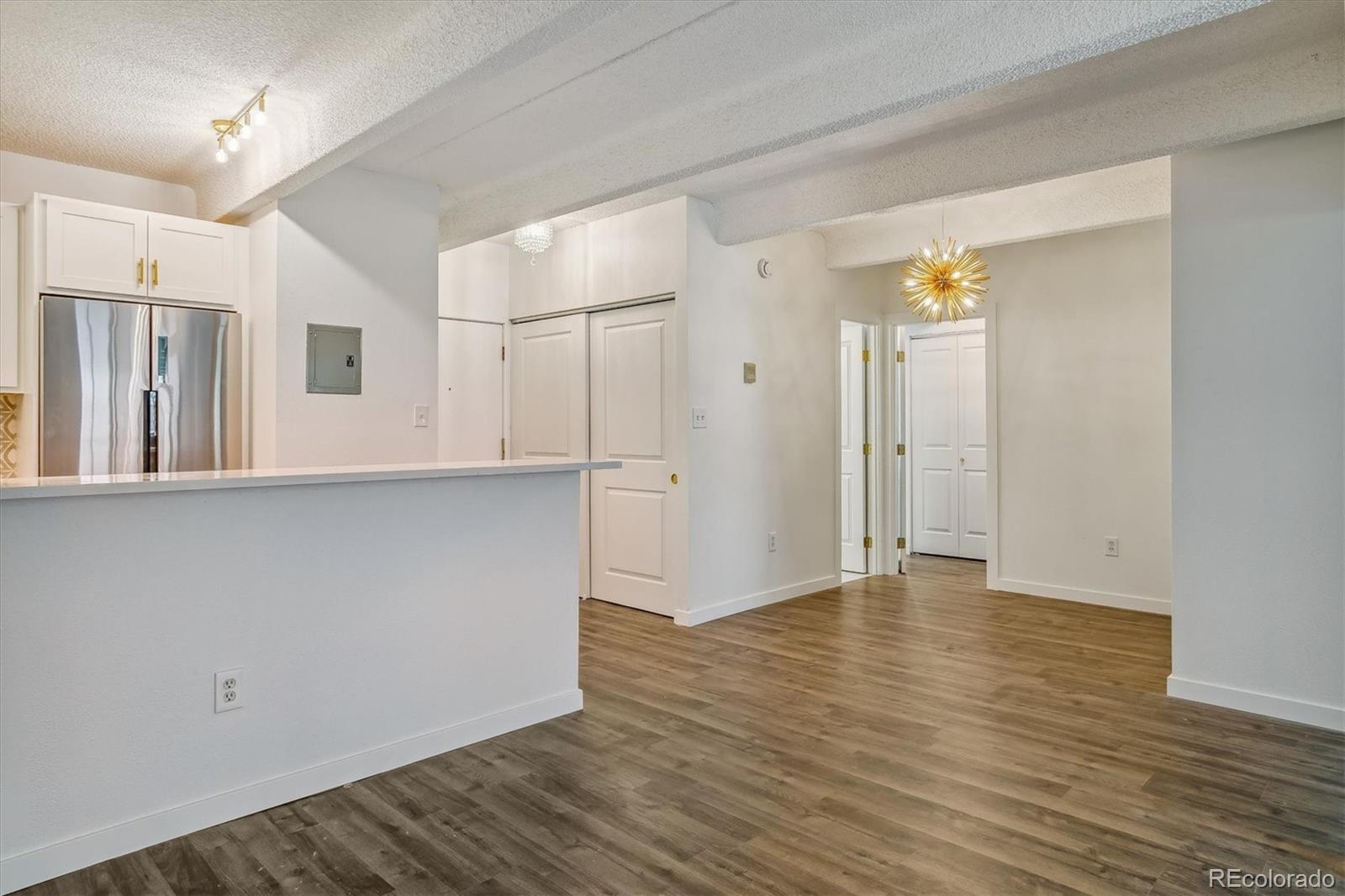 Vacant open kitchen and dining area with a white breakfast bar, stainless steel refrigerator, and wood-look floors.