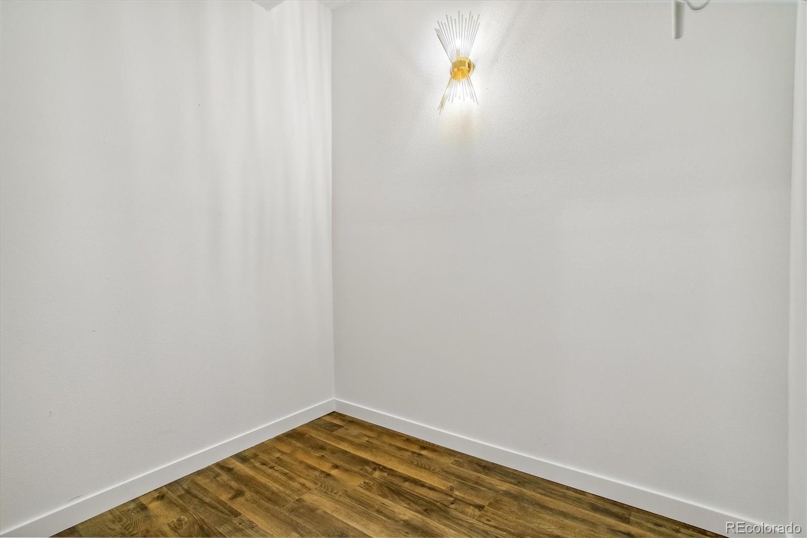 Empty room corner with wood-look flooring and a lit wall sconce.