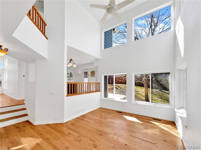 Two-story great room with hardwood floors, a ceiling fan, and large windows.