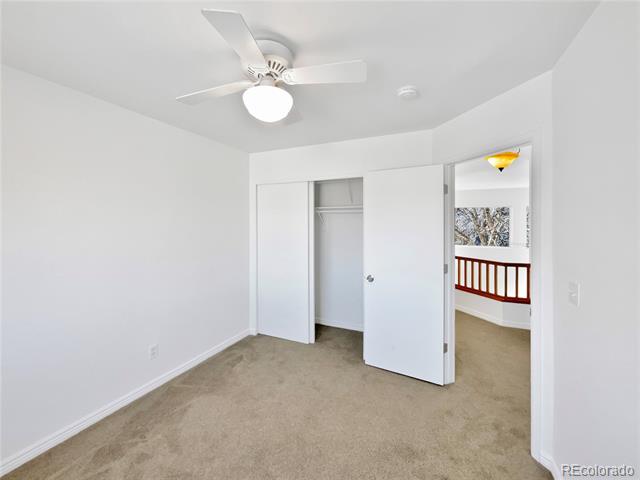 Empty bedroom with beige carpet, ceiling fan, and open closet doors.