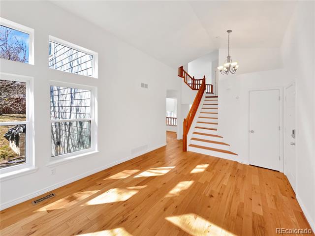 Bright entryway with hardwood floors, tall windows, and a staircase with a reddish wood railing.