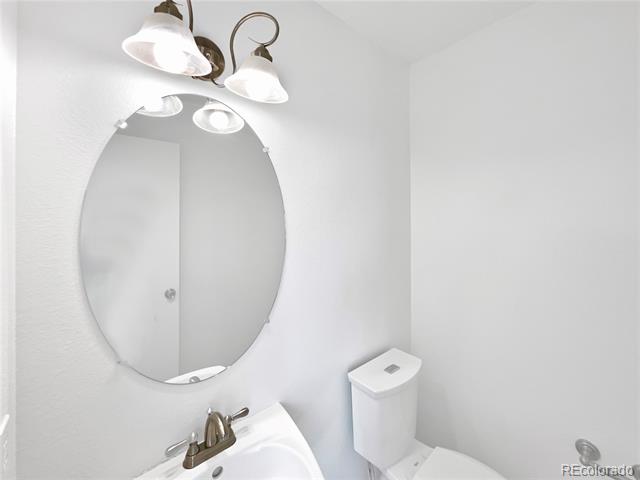 Bathroom with an oval mirror, white sink, bronze faucet, and toilet.