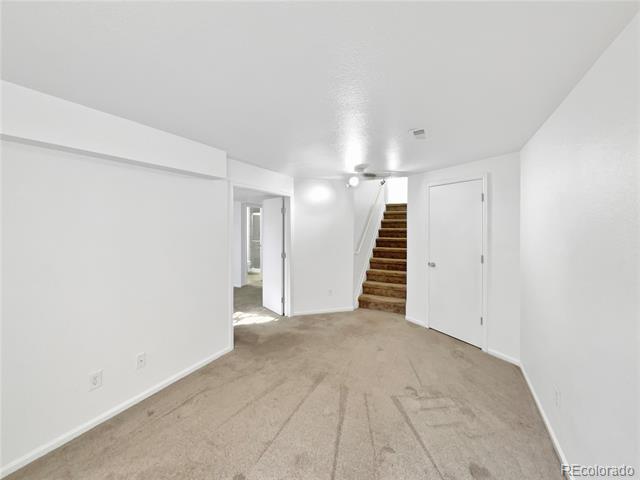 Basement room with beige carpet, a staircase, and an open doorway to an adjoining room.