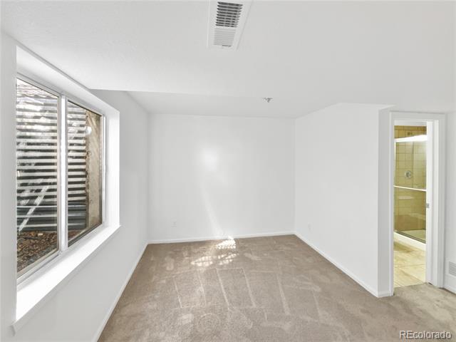 Empty carpeted bedroom with a large window and an open doorway to a tiled bathroom.