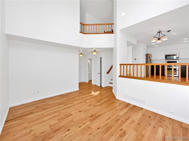 Open living area with hardwood floors, a vaulted ceiling, and a view into the kitchen.