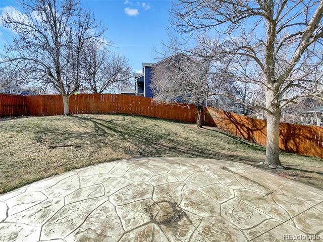 Fenced backyard with a stamped-concrete patio, dormant lawn, and leafless trees.