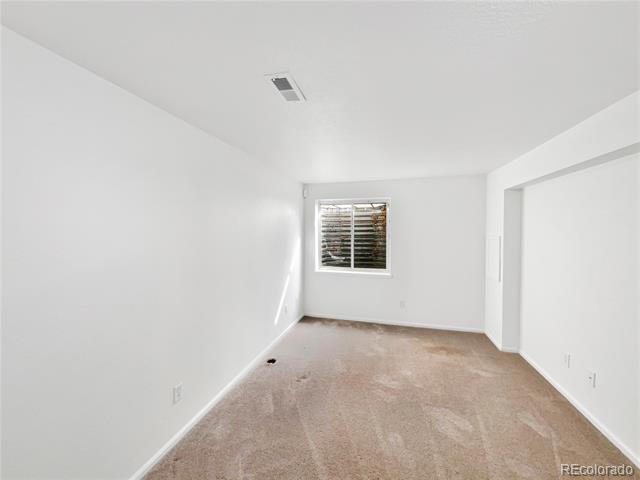 Empty bedroom with beige carpet, a small window with blinds, and an open closet area.