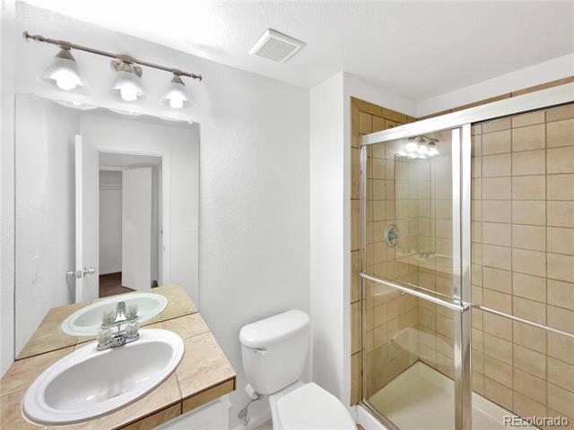 Bathroom with a tan tiled glass shower, vanity sink, and toilet.