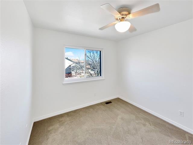 Empty bedroom with beige carpet, a ceiling fan, and a window overlooking leafless trees.