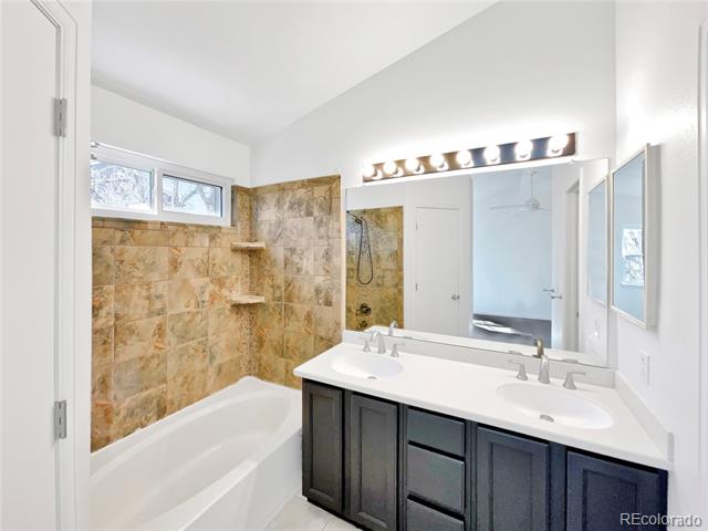 Bathroom with a tan stone-tile tub surround and dark double-sink vanity.